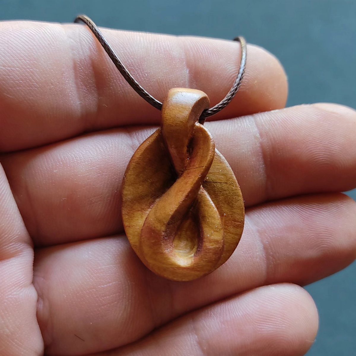 Art in Wood: 8 Ideas, From Knot Jewelry to Totem Pillars 3 Carved wooden knot pendant held in a person's hand on a brown cord
