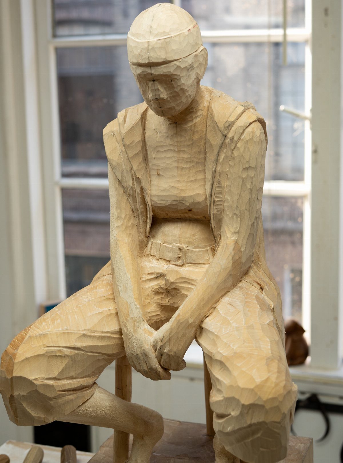 Art in Wood: 8 Ideas, From Knot Jewelry to Totem Pillars 6 Wooden sculpture of a seated person with visible carving marks in front of a window