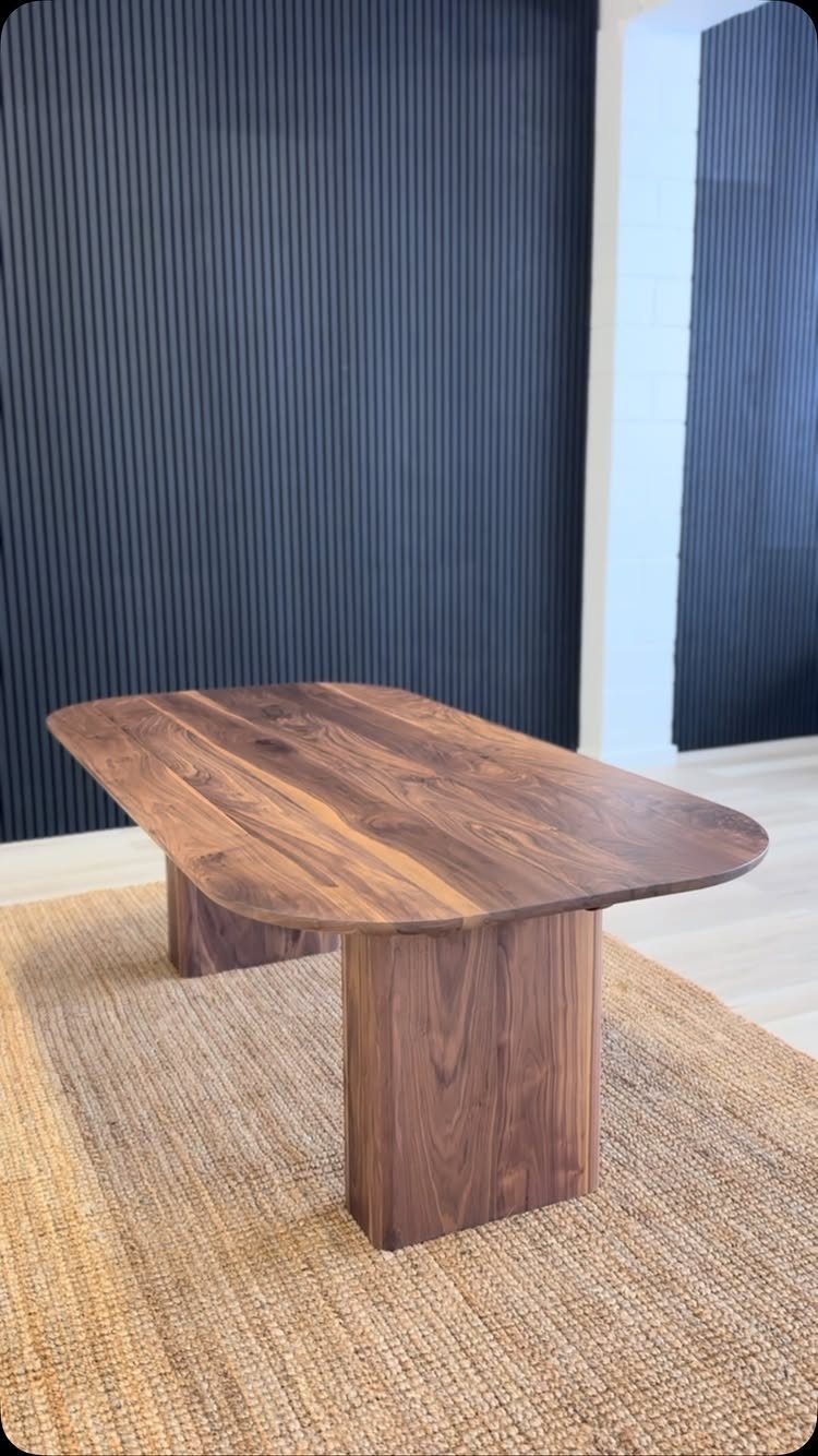 Organic shaped walnut wood dining table with block legs on a jute rug.