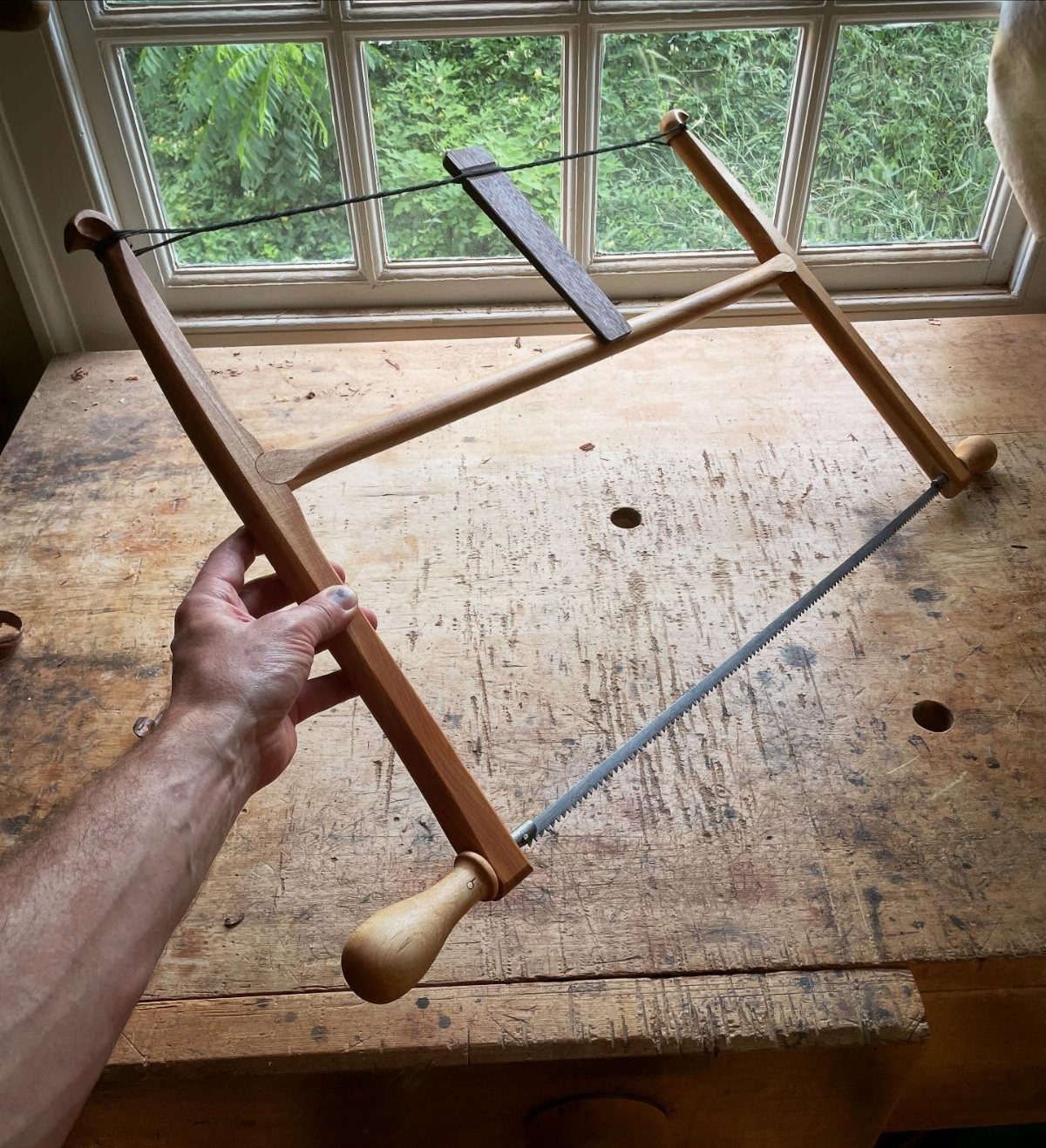 13 Carpentry Tools and Equipment for Every Workshop 13 Wooden bow saw held over a rustic workbench in a bright workshop.