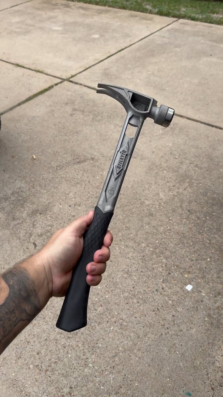 13 Carpentry Tools and Equipment for Every Workshop 1 Grey metal claw hammer with black grip held by a hand over concrete.