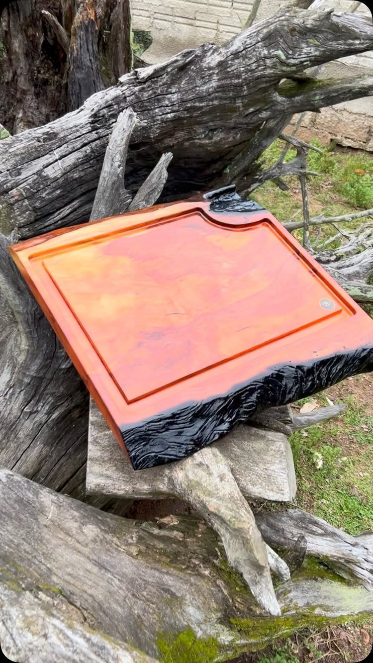 Wooden board with orange surface and black charred edge resting on driftwood.