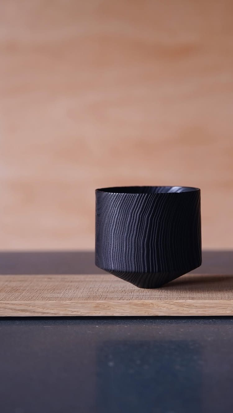 Charred wood cup with deep black texture on a light wooden surface