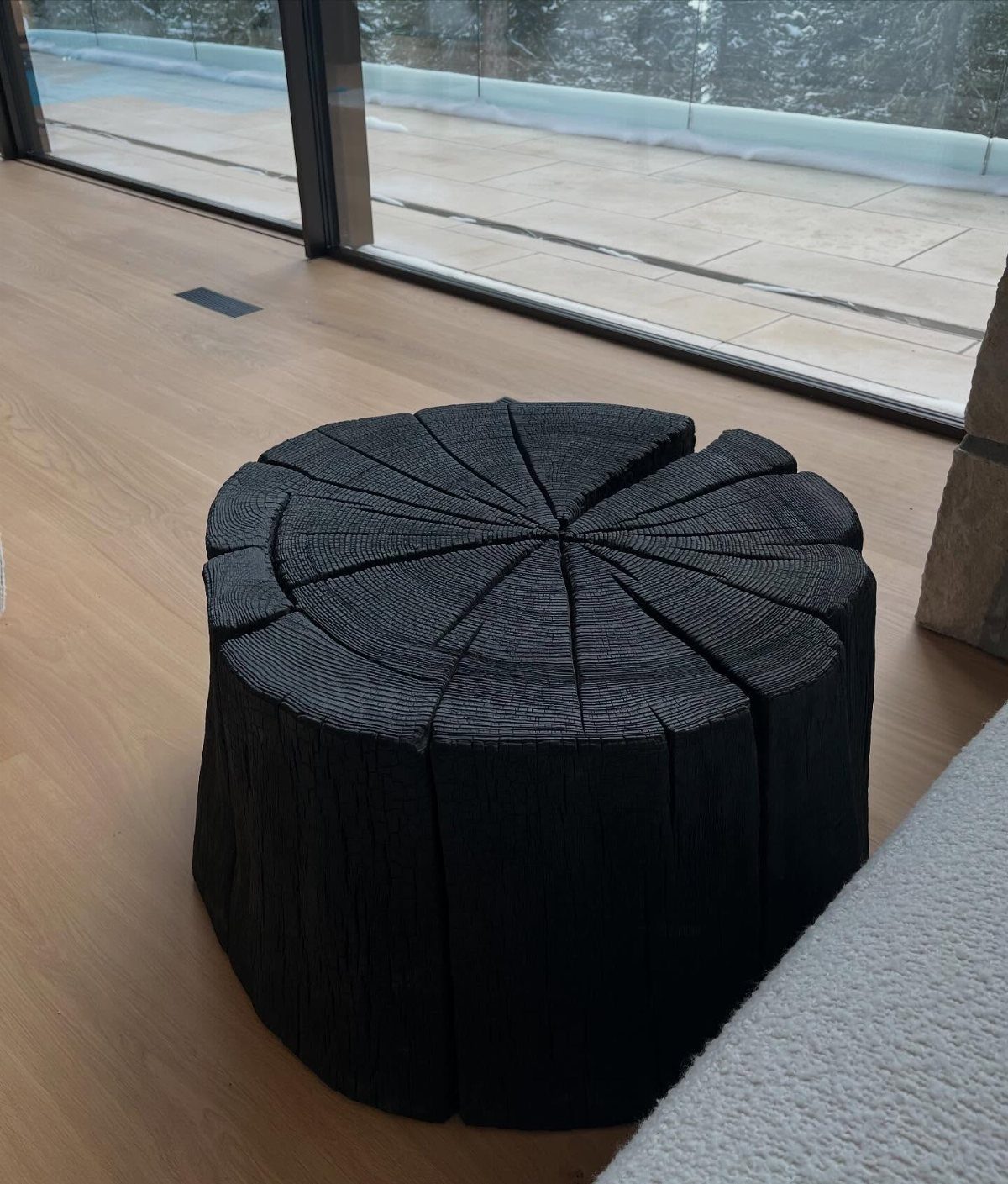 Charred black wood side table with radial slices on a light wood floor.
