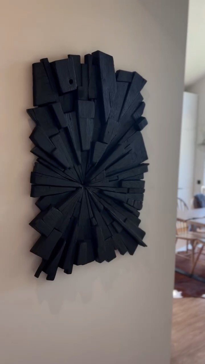 Charred black wood wall sculpture with radiating blocks on a white wall