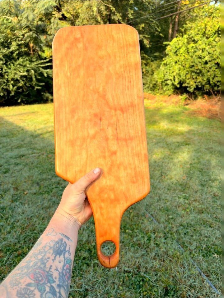 Cherry Wood Projects: 9 Ideas for Bowls, Boxes and More 4 Cherry wood charcuterie board held by a tattooed hand outdoors in a grassy area.
