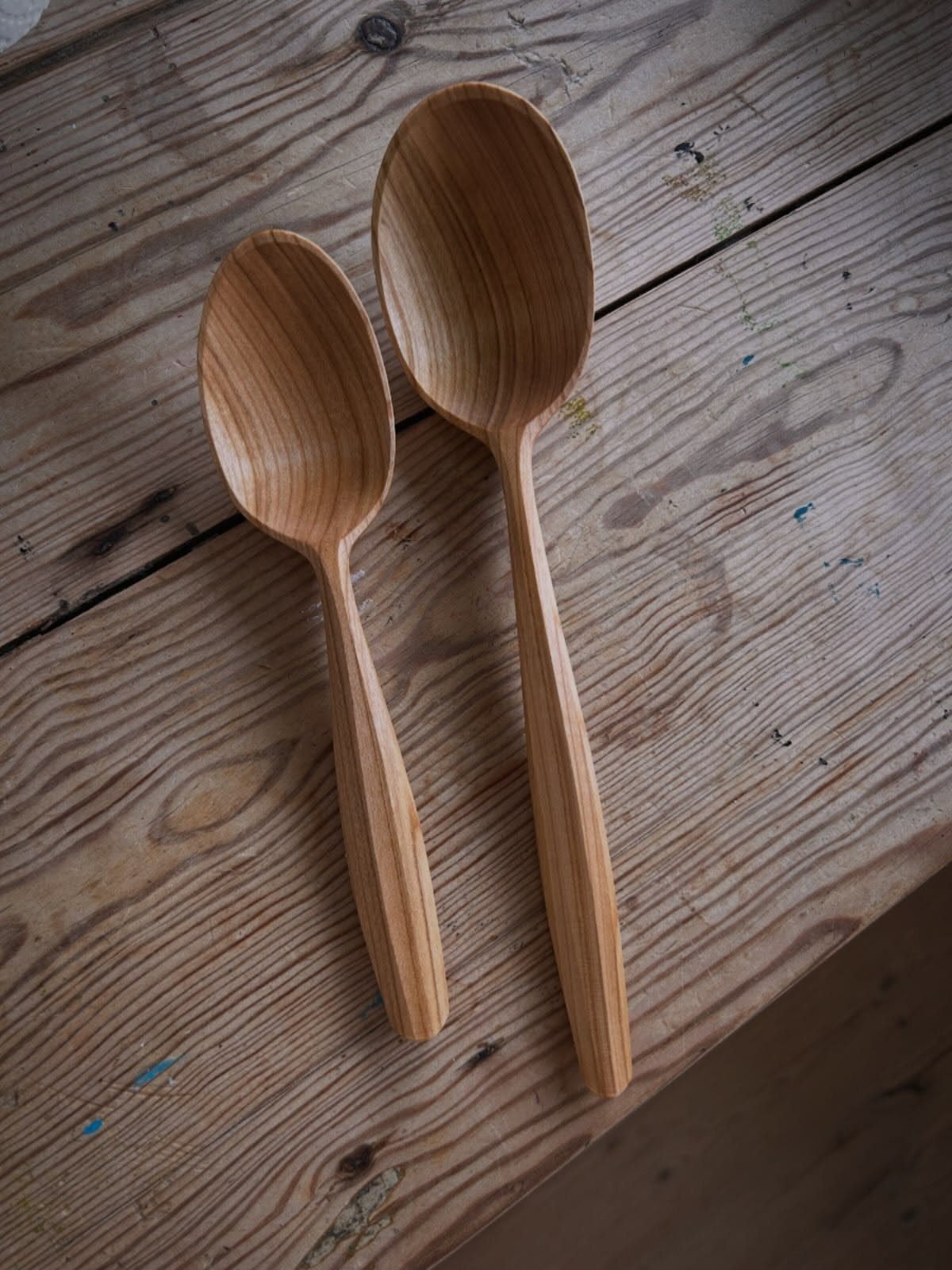 Cherry Wood Projects: 9 Ideas for Bowls, Boxes and More 5 Two hand-carved wooden spoons resting on a rustic weathered wood plank surface.