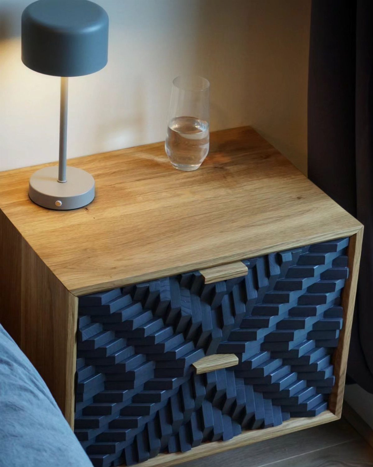 Creative Wood Designs: 8 Ideas for Furniture and Decor 3 Wooden bedside table with a blue geometric carved drawer and a grey lamp.