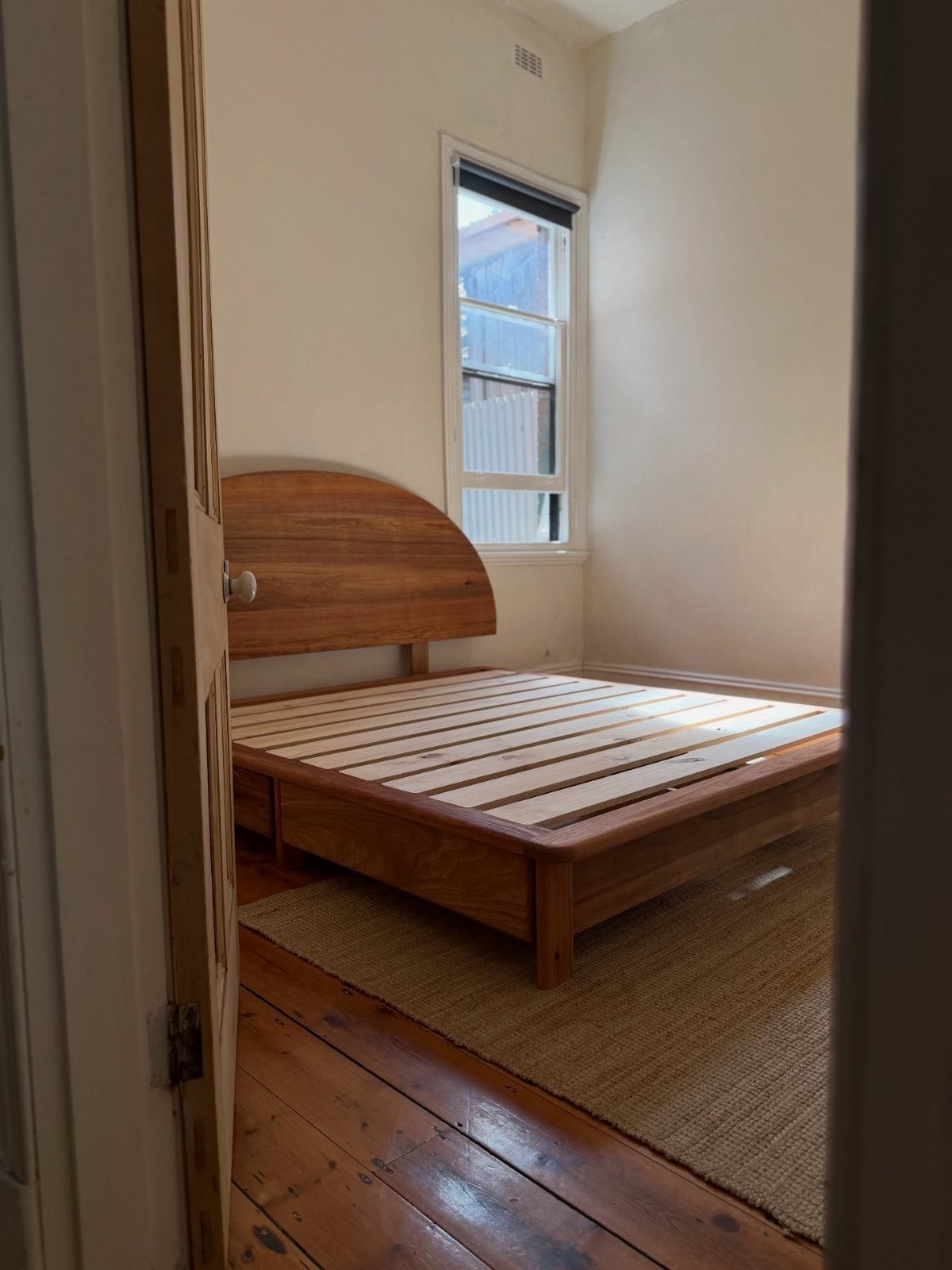 Wooden platform bed frame with a curved headboard in a bright bedroom