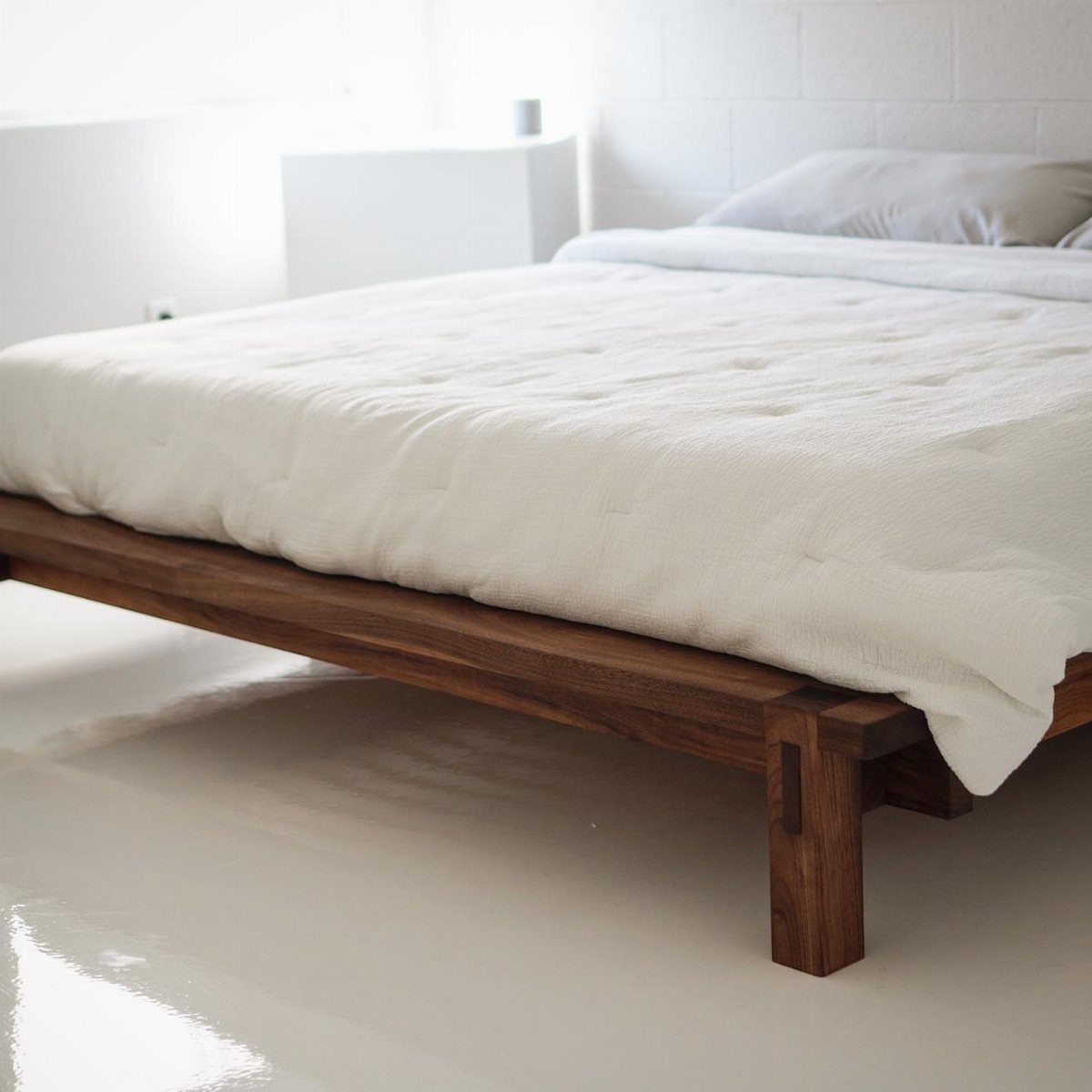 Dark brown wooden platform bed frame with white quilted bedding in a bright room.