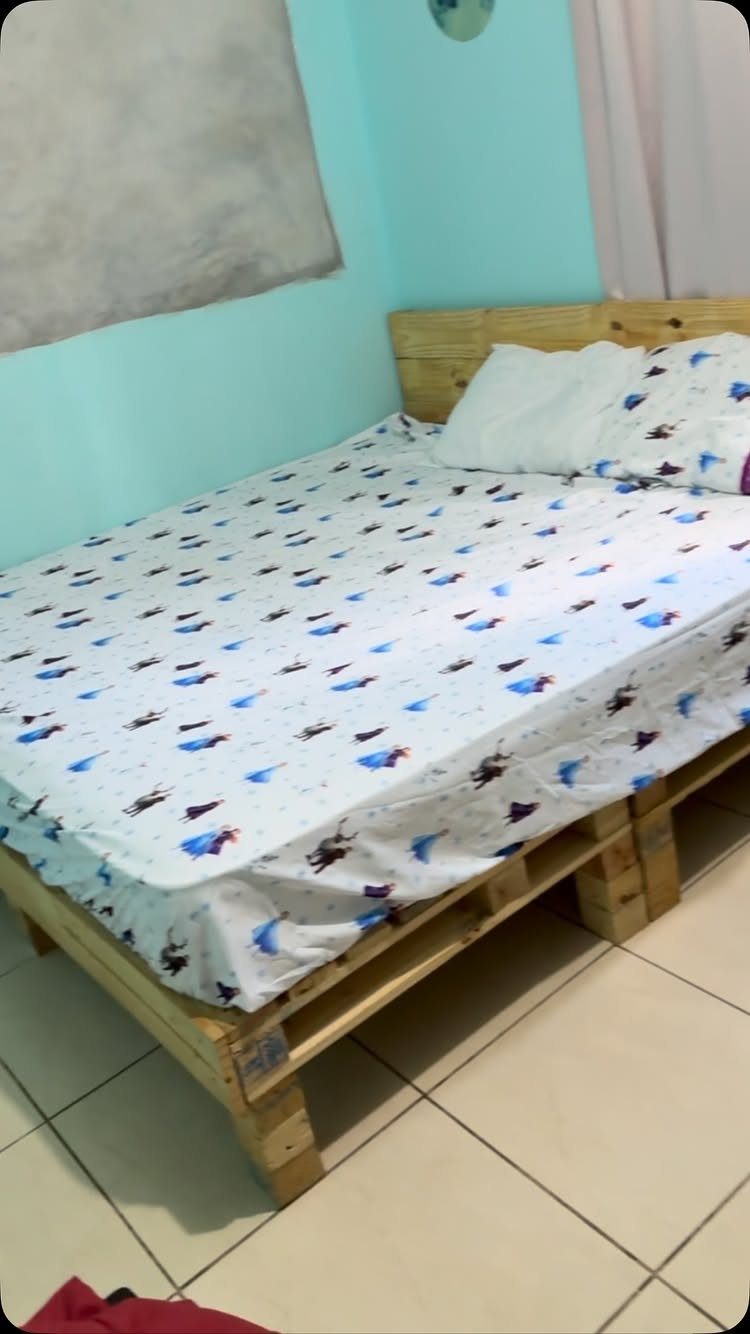 Wooden pallet bed frame with a white patterned mattress and pillows against blue walls.