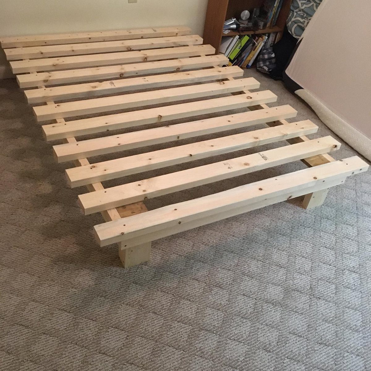 Handmade wooden bed frame with light pine slats on a grey carpeted floor