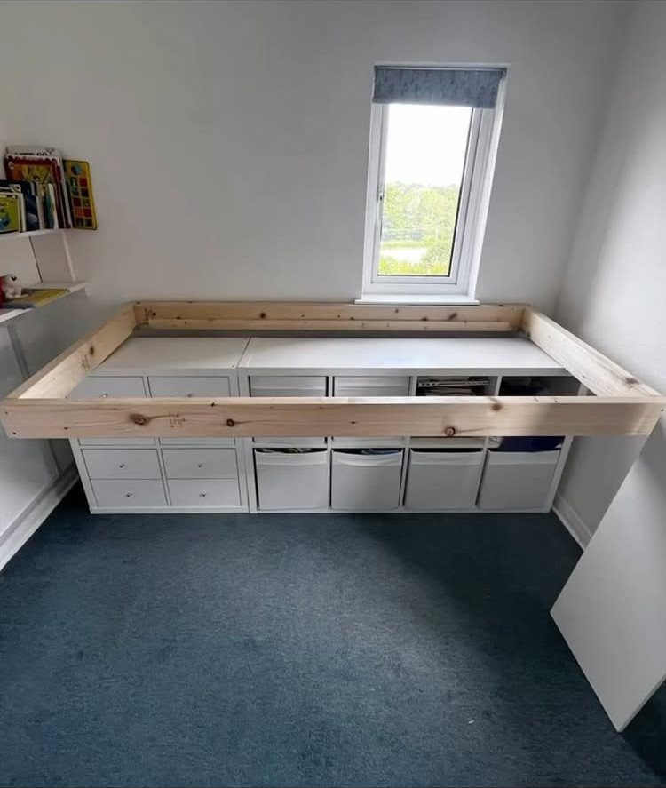 Wooden bed frame built over white storage drawers in a bright bedroom