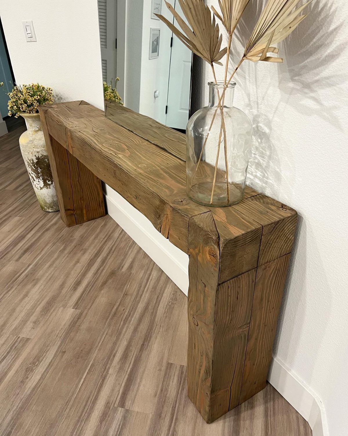 DIY Entryway Table Ideas and Plans: 4 Simple Builds 2 Rustic reclaimed wood console table with a glass vase of dried palm leaves.