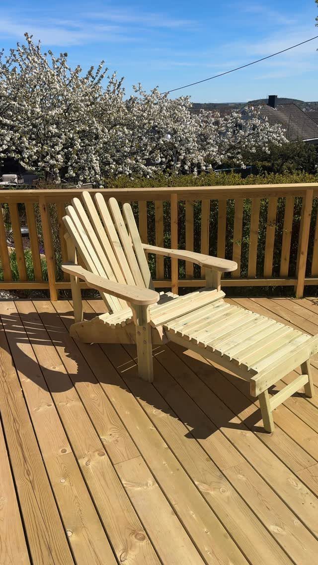 Wooden lounge chair with footrest on a sunny deck with blooming white trees.