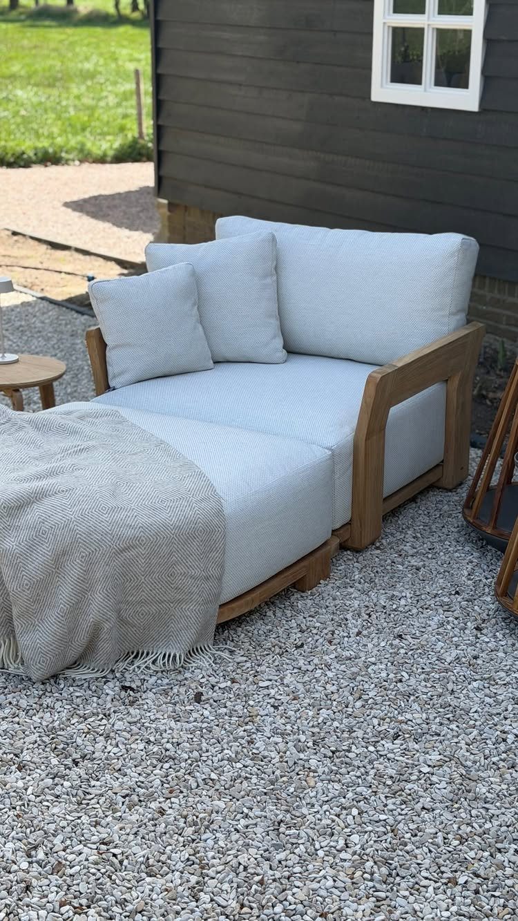 Modern outdoor lounge chair with light grey cushions and wooden frame on gravel.