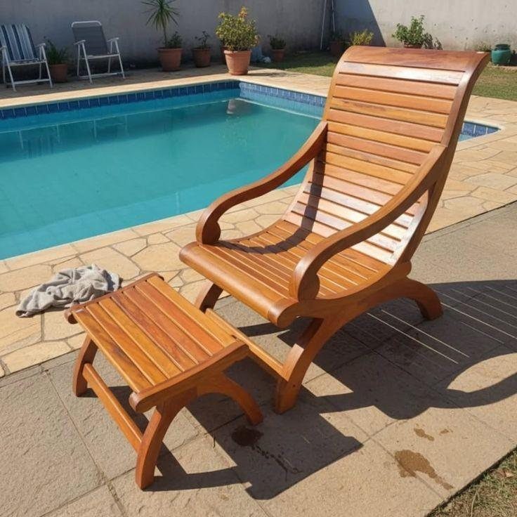 Wooden lounge chair and footstool on a stone patio beside a swimming pool.