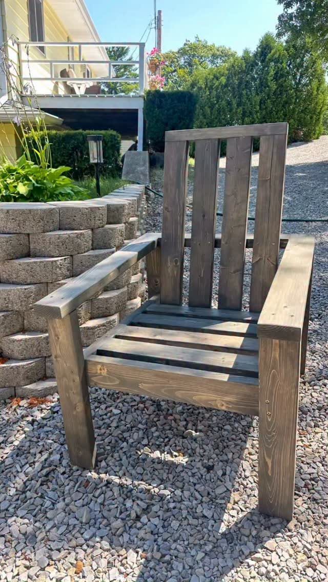 10 DIY Outdoor Chair Ideas for Patios, Porches and Decks 6 Dark brown wooden outdoor chair sitting on grey gravel next to a stone wall.