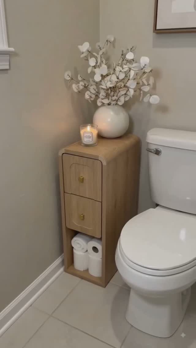 Narrow light wood bathroom cabinet with toilet paper rolls on the bottom shelf.