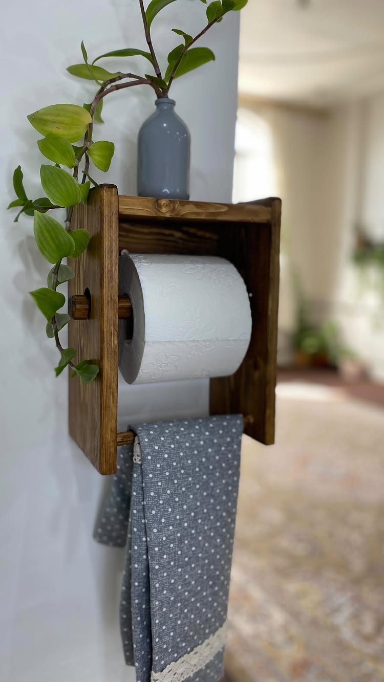 Wooden box toilet paper holder with a grey polka-dot towel and small plant.