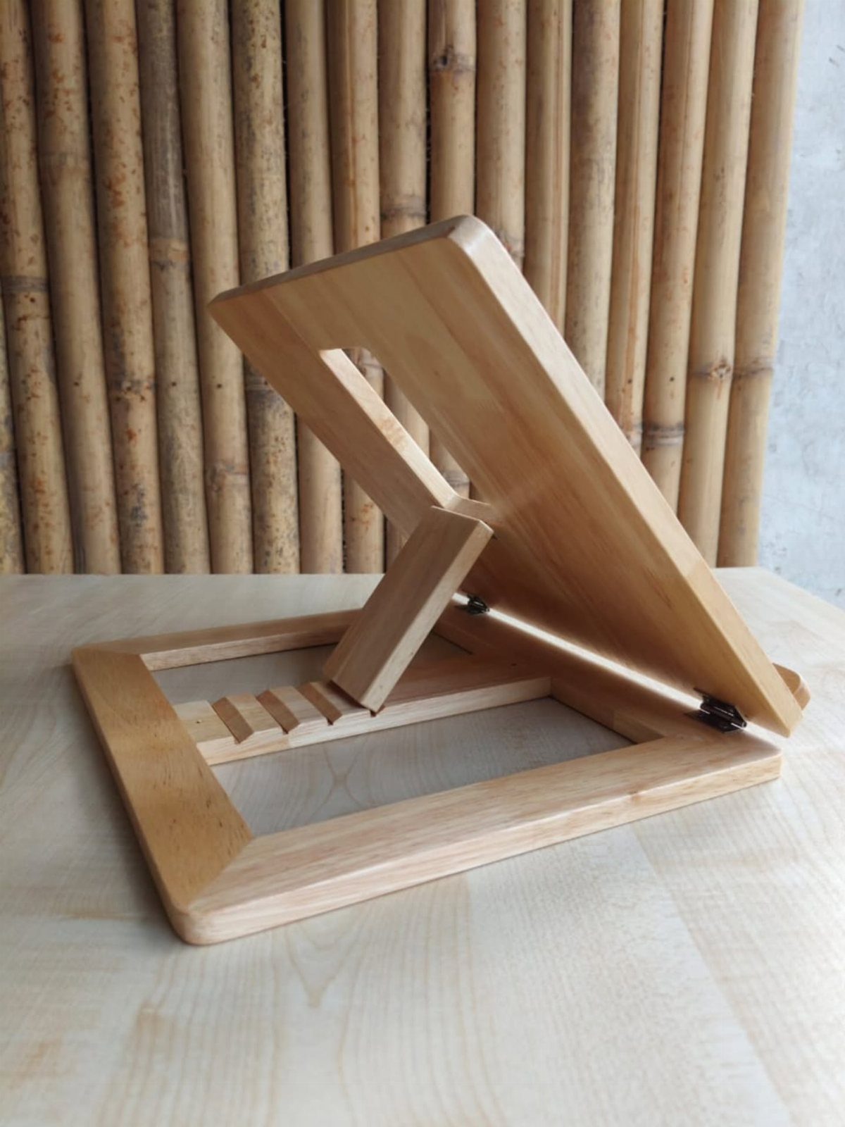 Wooden book stand with adjustable backrest on a light table against bamboo poles.