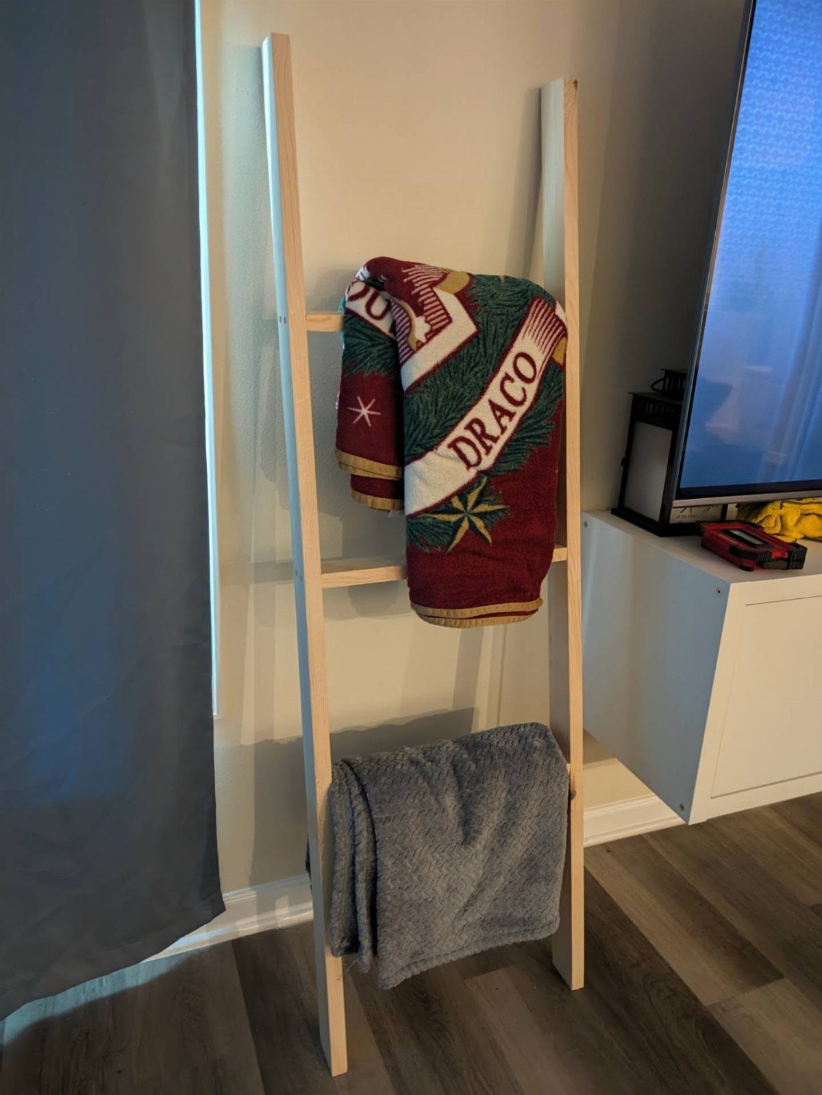 Wooden blanket ladder leaning against a wall with two blankets draped over it.