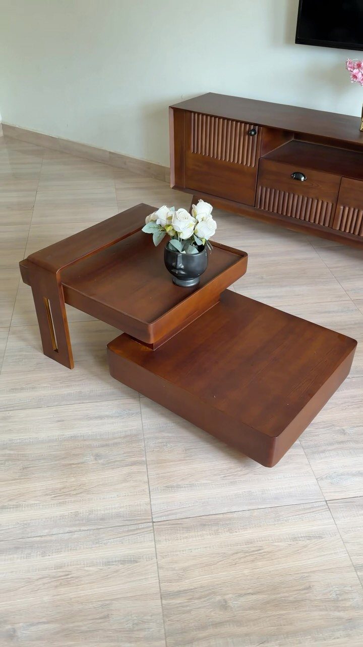 Two-tiered brown wooden coffee table with white flowers on a tiled floor.