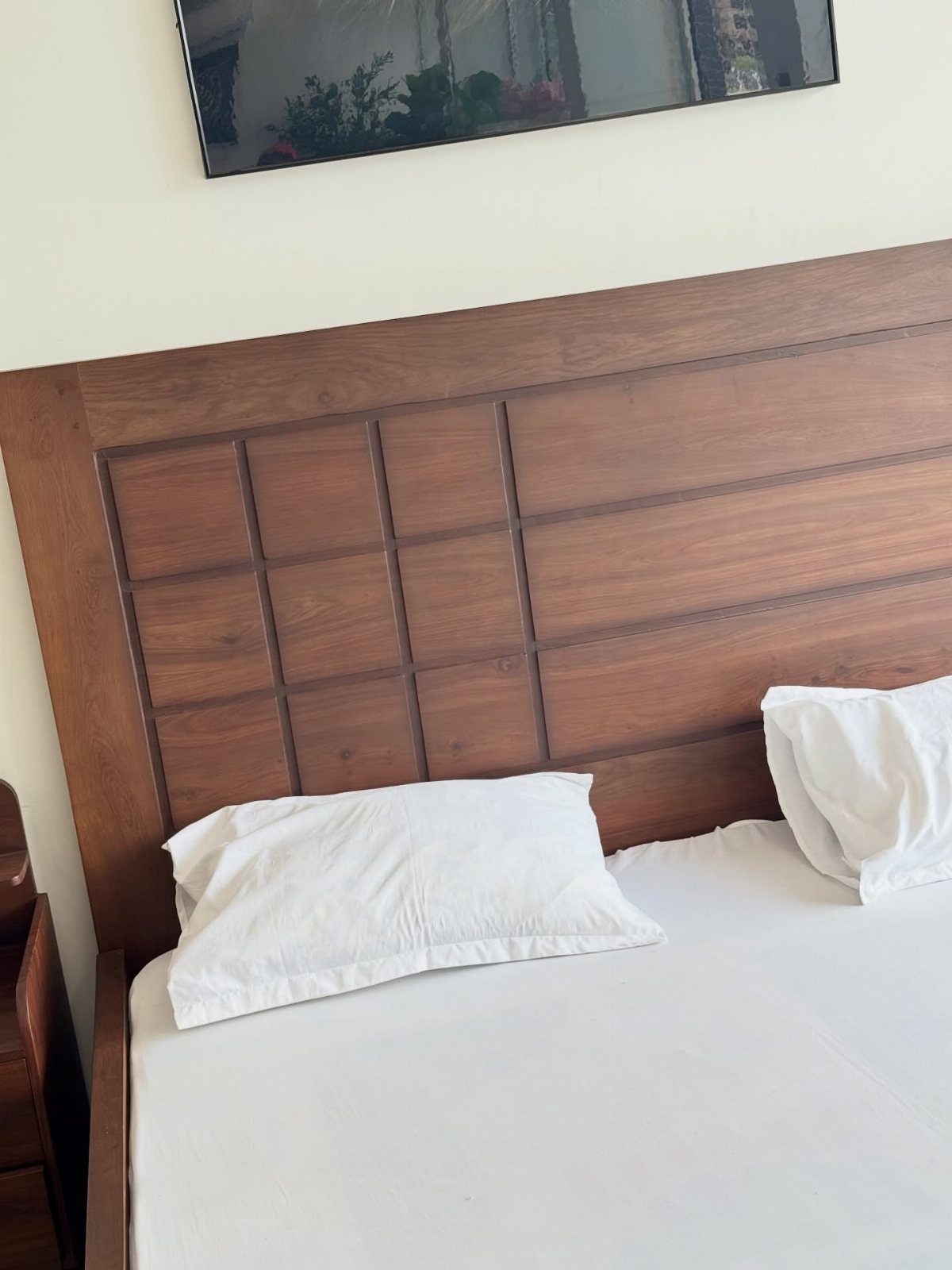 Brown wooden paneled headboard behind a bed with white pillows and sheets.