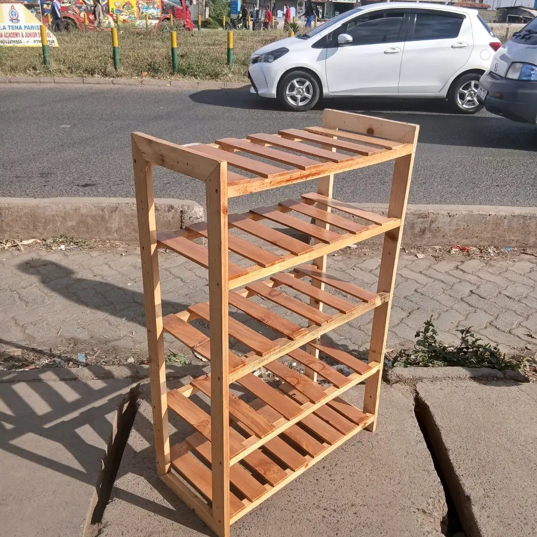 Wooden shoe rack with five slatted shelves standing on a paved city sidewalk.