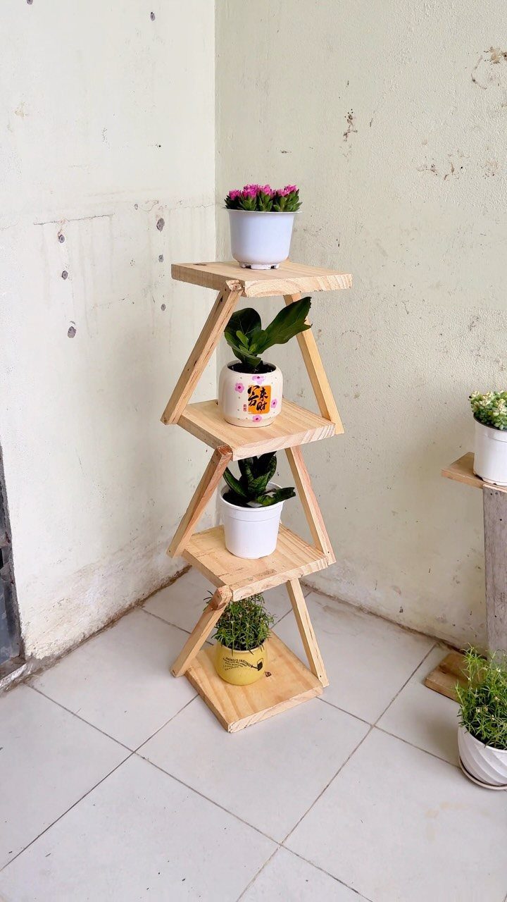 Three-tiered light wood plant stand holding various potted green plants and flowers.