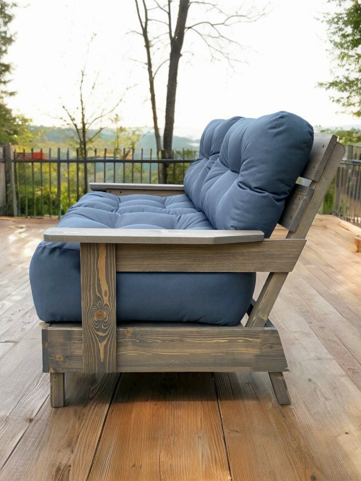 Grey wooden outdoor sofa with blue cushions on a sunny wooden deck.
