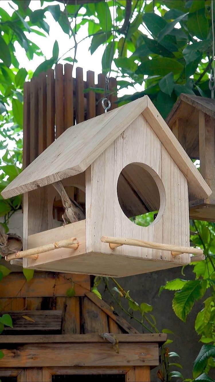 16 DIY Wooden Projects for Home, Garden, and Holiday Decor 10 Wooden birdhouse with a peaked roof hanging among green garden leaves.