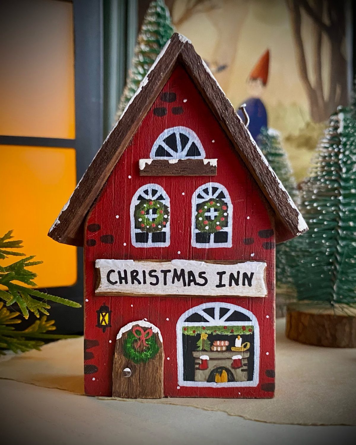 16 DIY Wooden Projects for Home, Garden, and Holiday Decor 13 Red wooden Christmas Inn model house with snow on the roof and festive wreaths.