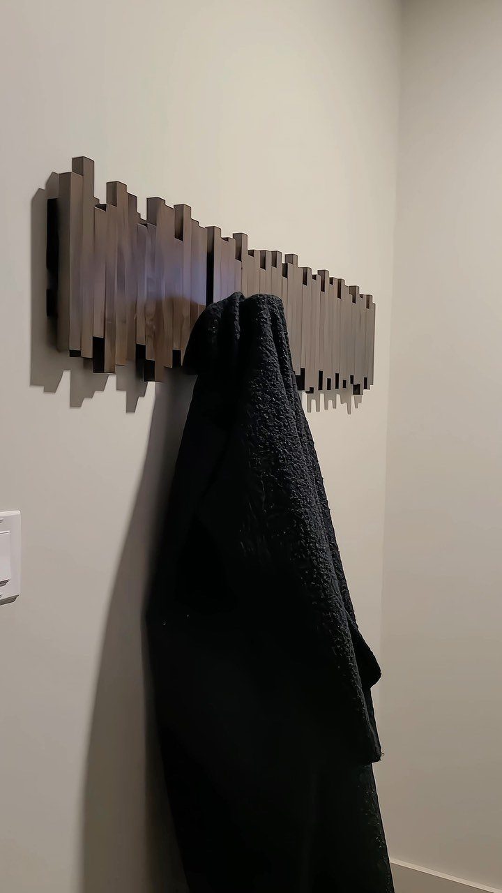 16 DIY Wooden Projects for Home, Garden, and Holiday Decor 3 Geometric dark brown wooden coat rack mounted on a wall holding a black garment.