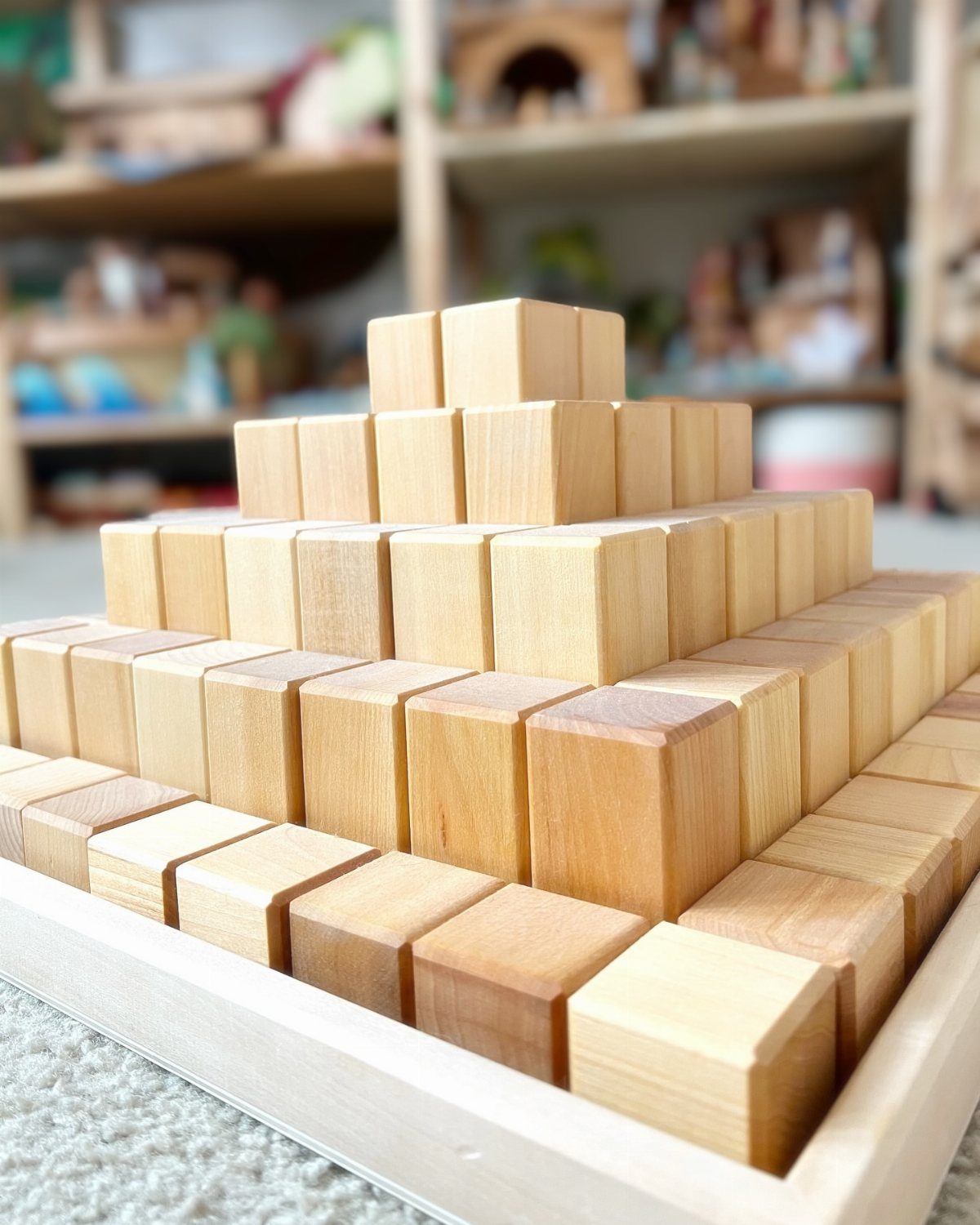 16 DIY Wooden Projects for Home, Garden, and Holiday Decor 15 Wooden cubes stacked in a pyramid shape inside a light wood tray.