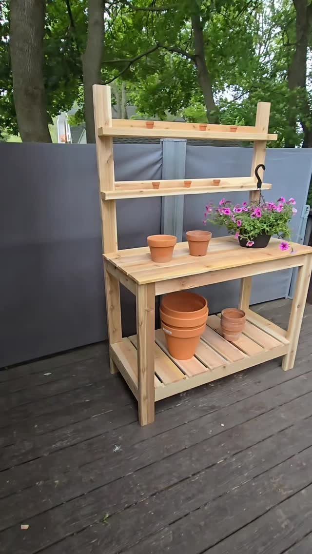 16 DIY Wooden Projects for Home, Garden, and Holiday Decor 16 Wooden outdoor potting bench with terracotta pots and pink flowers on a deck.