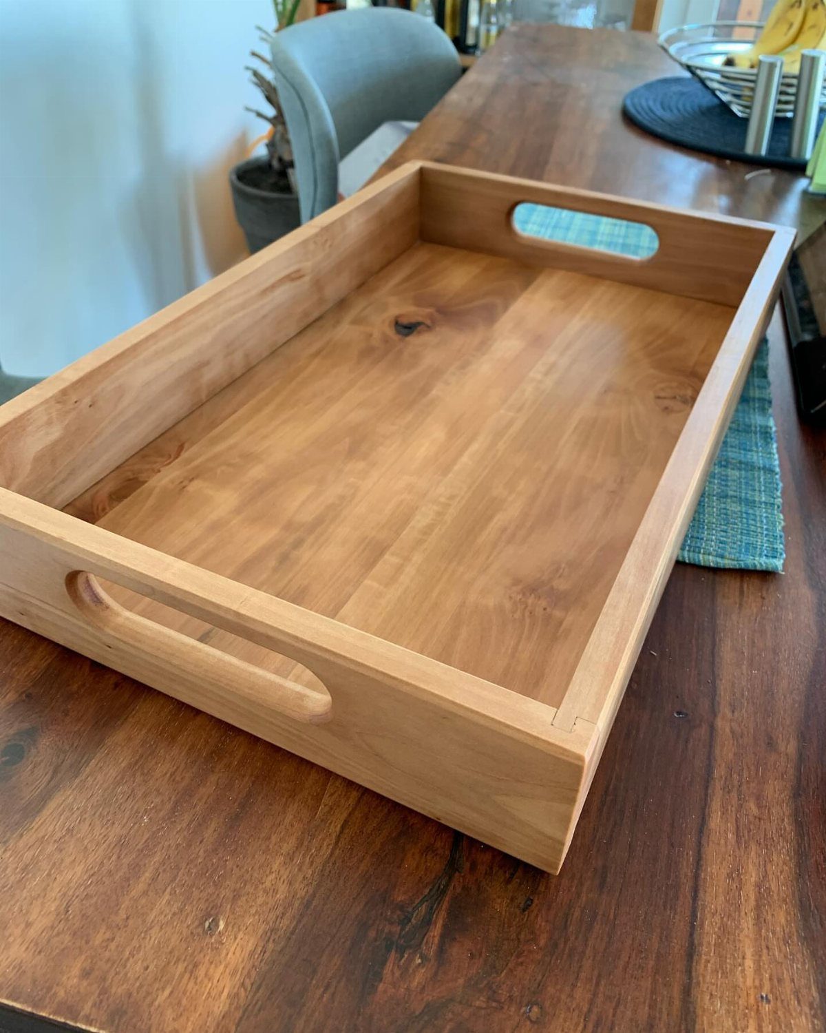 16 DIY Wooden Projects for Home, Garden, and Holiday Decor 4 Wooden serving tray with handle cutouts sitting on a dark wood table.