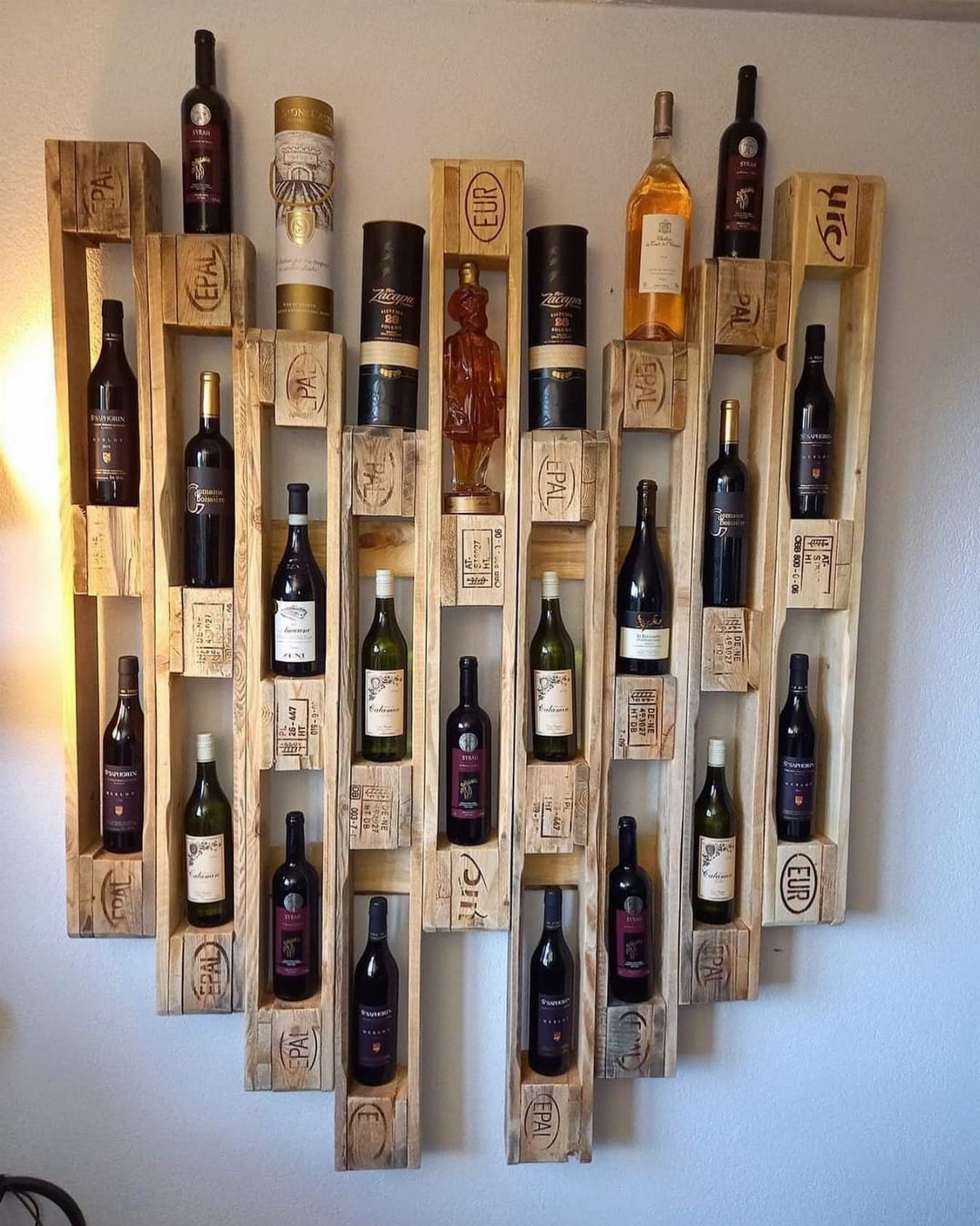 16 DIY Wooden Projects for Home, Garden, and Holiday Decor 7 Wooden pallet wine rack mounted on a white wall holding several wine bottles.