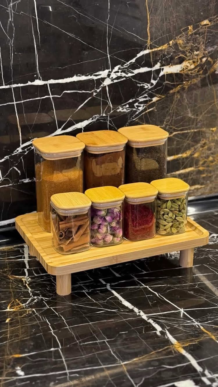 6 DIY Wooden Riser Ideas for Plants, Kitchens and Decor 4 Wooden riser holding glass spice jars on a black marble kitchen countertop.