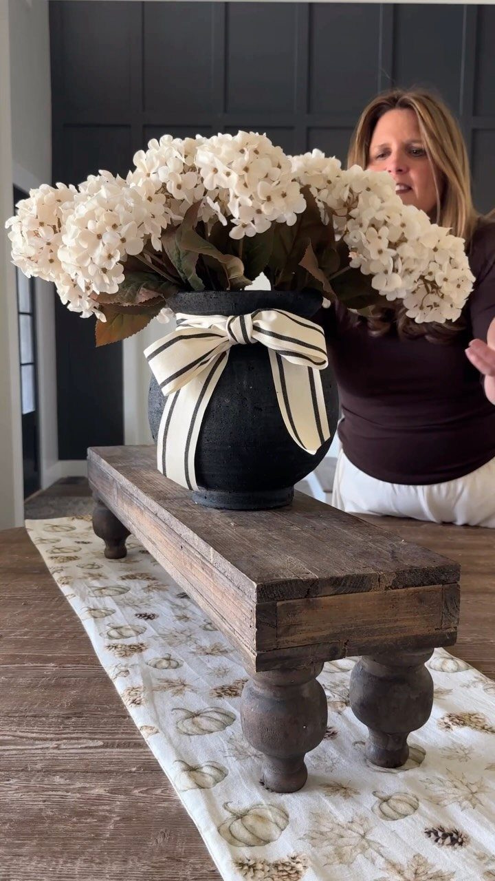 6 DIY Wooden Riser Ideas for Plants, Kitchens and Decor 5 Rustic wooden riser with turned legs holding a black vase of white flowers.