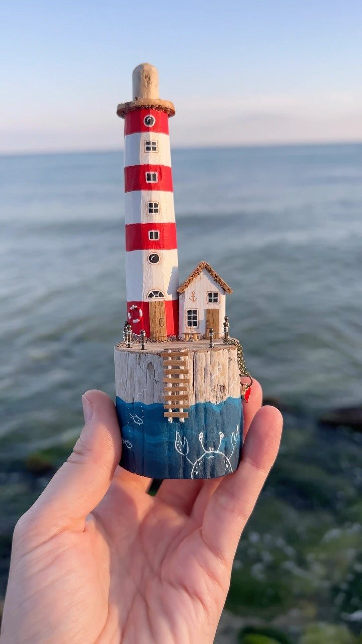 Hand-carved driftwood lighthouse sculpture with red and white stripes by the ocean.