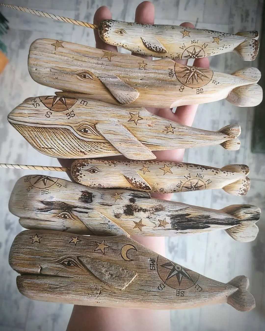 Six carved wooden whales with compass and star details held in a hand.
