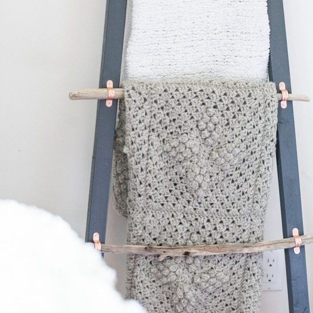 Driftwood blanket ladder with grey and white blankets leaning against a white wall.