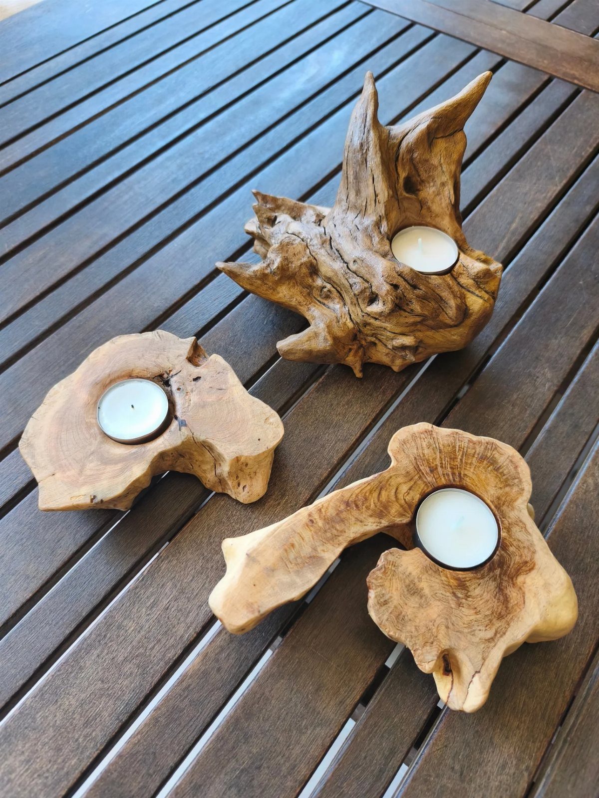 Three tea light candles nestled in natural driftwood holders on a wooden table.