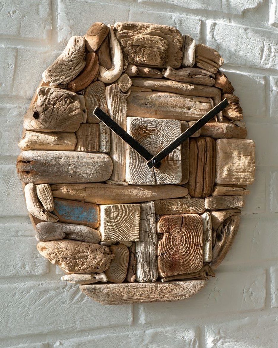 Driftwood clock with black hands mounted on a white brick wall.