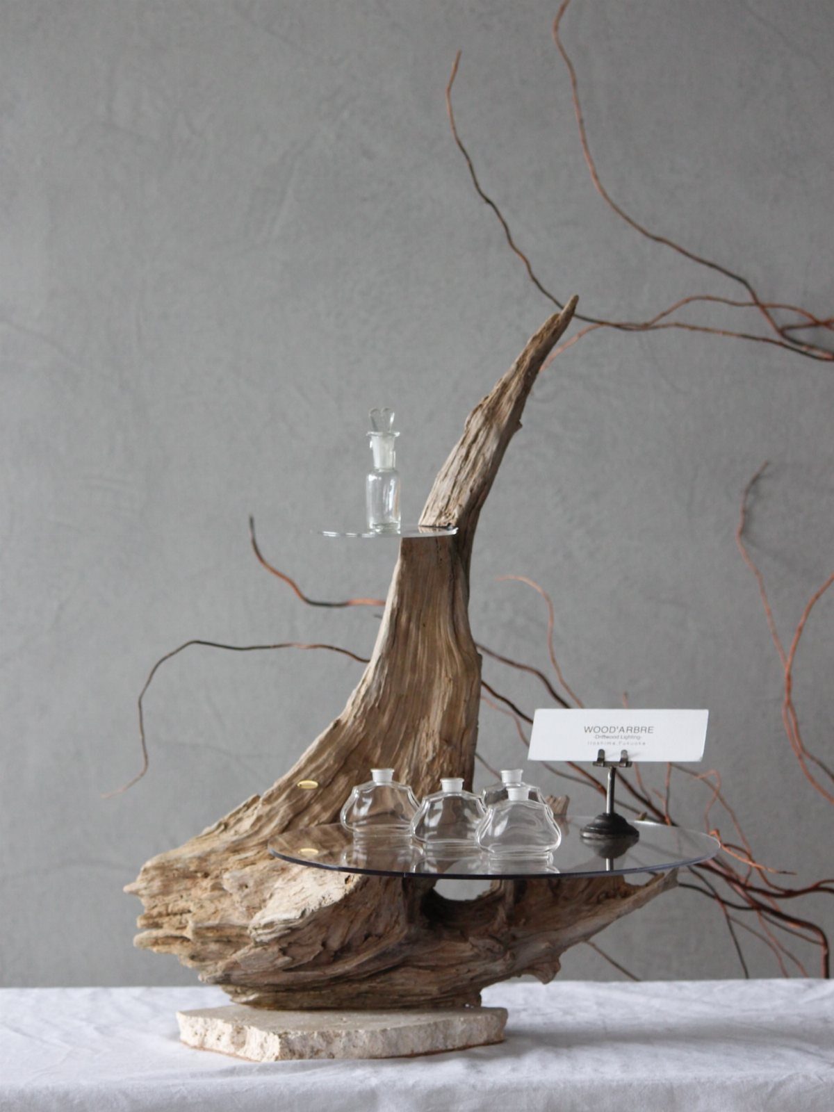 Driftwood display stand with glass shelves holding small clear glass bottles.