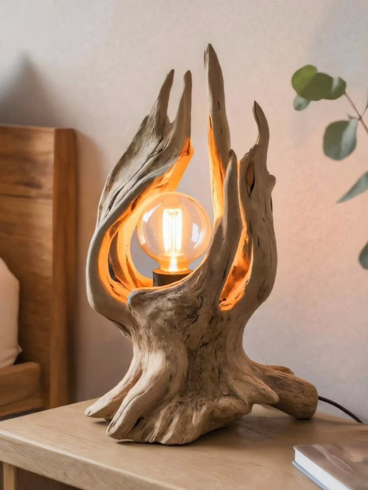 Driftwood lamp with a glowing round bulb resting on a wooden bedside table.