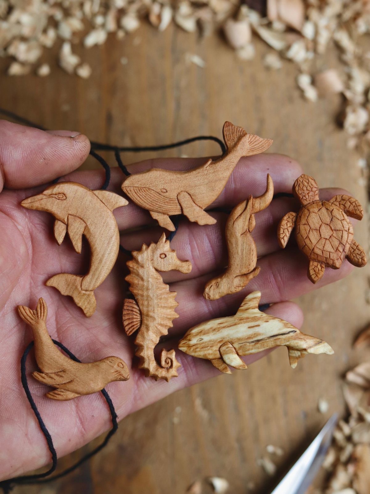 Small carved wooden sea creature ornaments held in a person's hand over wood shavings.
