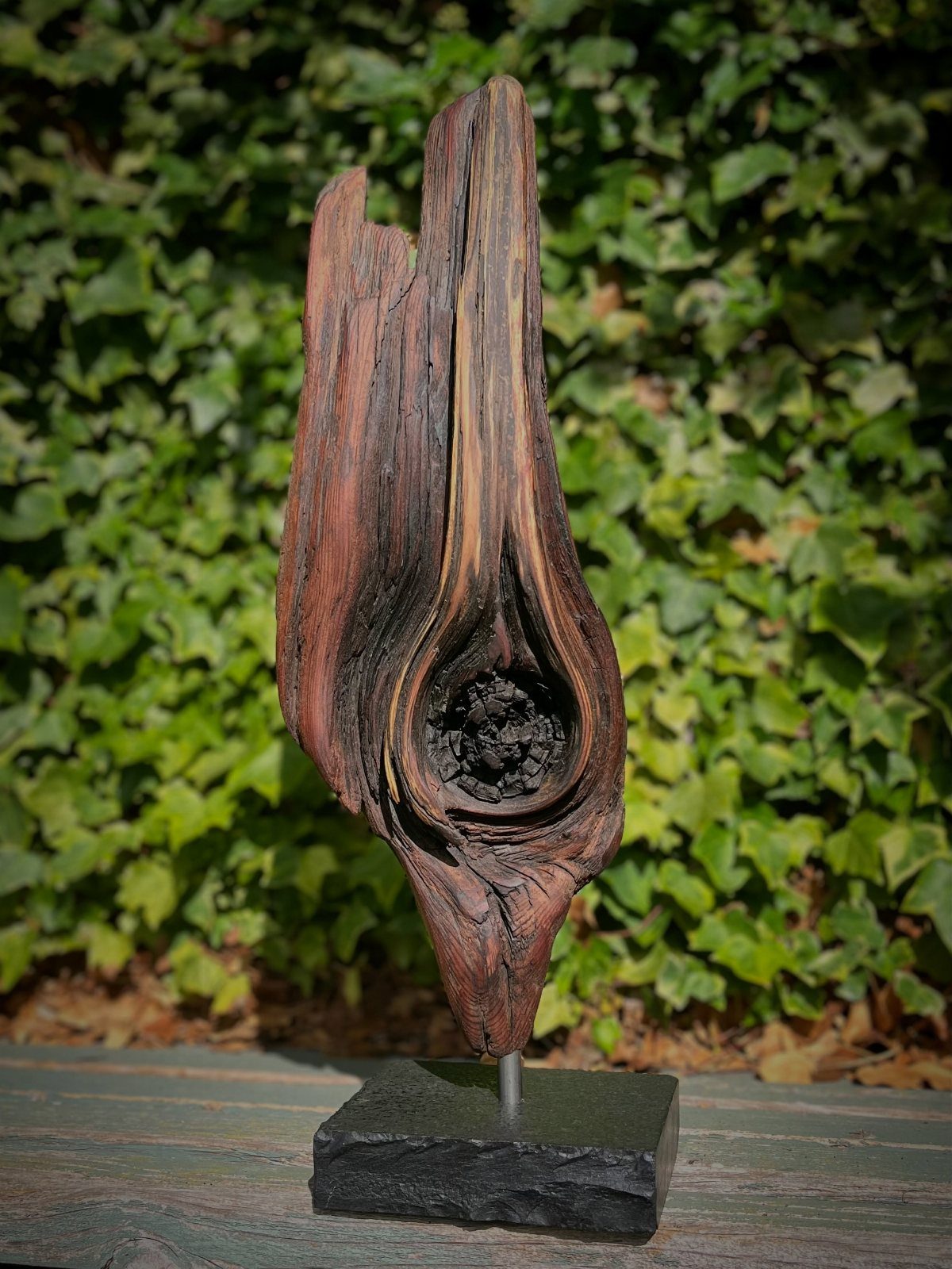 Weathered brown driftwood sculpture with a natural knot on a black base.