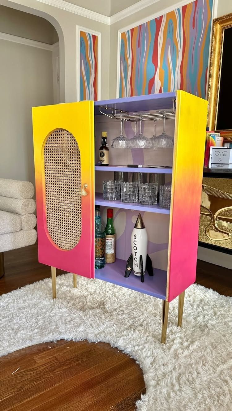 Gradient painted drinks cabinet with caned door and gold legs on white rug.